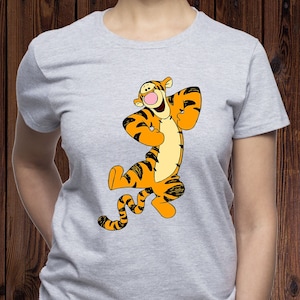 Könnte beinhalten: Ein graues T-Shirt mit einem Cartoon-Bild eines lächelnden orange-schwarz gestreiften Tigers mit einem schwarzen Schwanz. Der Tiger steht auf seinen Hinterbeinen mit erhobenen Vorderpfoten.