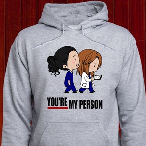May include: Gray hooded sweatshirt with a graphic of two cartoon figures wearing scrubs and the text "YOU'RE MY PERSON".