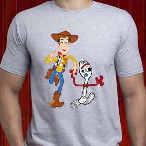 May include: A light grey t-shirt with a colourful graphic of Woody and Forky from Toy Story. Woody is in cowboy attire, and Forky is a white spork with red arms and a blue eye.