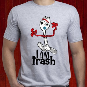 May include: A light grey t-shirt with a cartoon fork character with red arms and headband, and a blue mouth. The text "I AM trash" is printed below the character in black. The design is a fun, playful graphic.