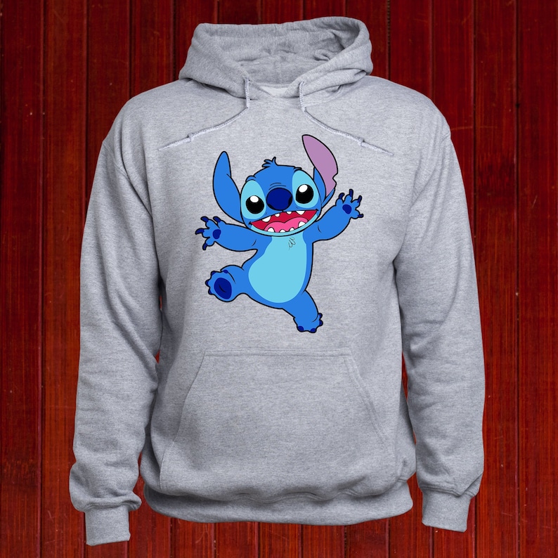 Puede incluir: Una sudadera con capucha gris con un personaje de dibujos animados azul de Stitch de Lilo & Stitch en la parte delantera. Stitch est&aacute; sonriendo y tiene los brazos extendidos.