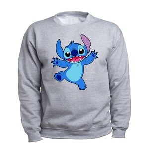 Puede incluir: Una sudadera gris con un personaje de dibujos animados azul de Stitch de la pel&iacute;cula de Disney Lilo & Stitch. Stitch est&aacute; sonriendo y tiene los brazos extendidos.