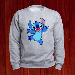 Puede incluir: Una sudadera gris con un personaje de dibujos animados azul de Stitch de Lilo & Stitch. Stitch est&aacute; sonriendo y tiene los brazos extendidos.