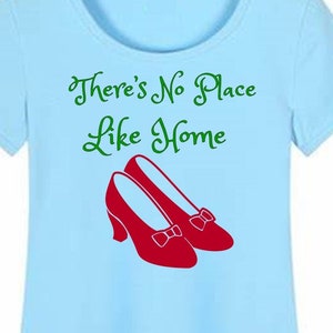 May include: Light blue t-shirt with a green graphic that says "There's No Place Like Home" and a pair of red ruby slippers.