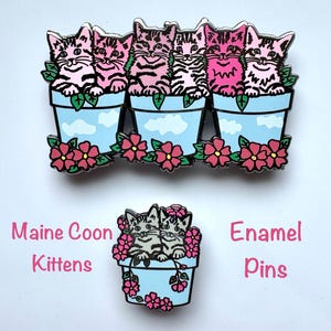 May include: Enamel pins depicting Maine Coon kittens in light blue flower pots with pink flowers. The pins have a black outline and the text "Maine Coon Kittens" and "Enamel Pins" in pink.