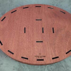 May include: Oval-shaped wooden tray with a reddish-brown finish. The tray has several evenly spaced, rectangular black inlays around the perimeter and in the center. The text "True North Wood Designs" is visible on the bottom right.