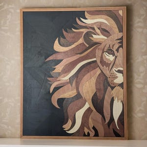 May include: A wooden wall art piece featuring a lion's head with a detailed mane made of different wood types. The lion's head is facing the right side of the image, and the mane is made of various shades of brown, beige, and cream wood. The background is a dark, geometric pattern made of black wood.