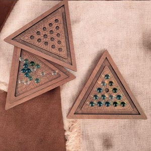May include: Wooden triangular game boards with intricate carved designs. Each board holds colorful glass marbles. The boards are arranged on a textured surface, creating a visually appealing arrangement. A classic game for all ages.
