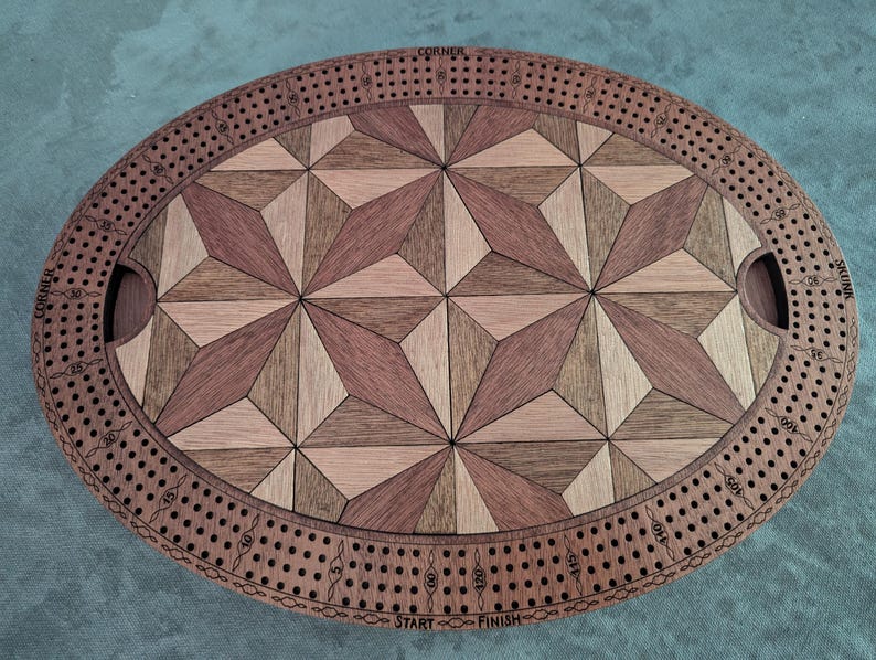 May include: Oval wooden cribbage board with a geometric starburst design in shades of brown and tan. The board has a track for pegs and cut-out handles. The words "CORNER", "SKUNK", "START", and "FINISH" are visible.