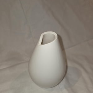 May include: A white, teardrop-shaped vase with a unique, asymmetrical opening. The ceramic vase has a smooth, glossy finish and a minimalist design, suitable for displaying flowers or as a decorative accent piece.