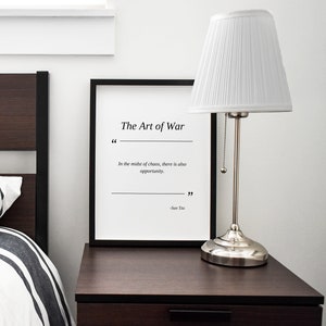 May include: A black framed print with a white background and the text "The Art of War" in black. The quote "In the midst of chaos, there is also opportunity." is printed below the title. The quote is attributed to "Sun Tzu" at the bottom of the print.