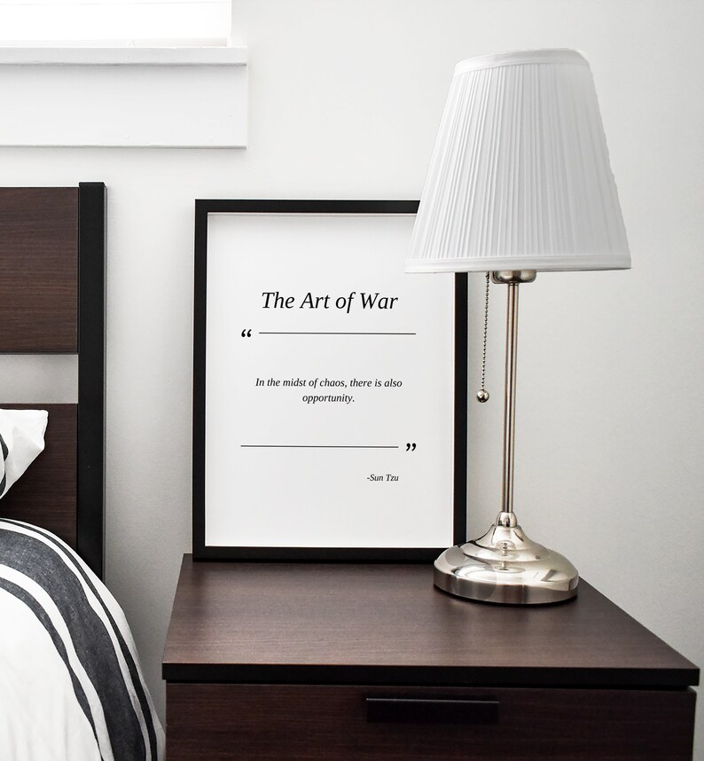 May include: A black framed print with a white background and the text "The Art of War" in black. The quote "In the midst of chaos, there is also opportunity." is printed below the title. The quote is attributed to "Sun Tzu" at the bottom of the print.