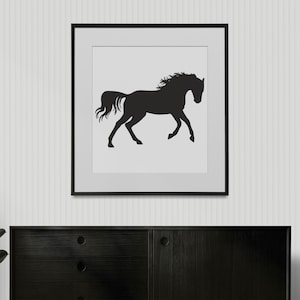 May include: A square wall art piece featuring a black silhouette of a horse in motion against a plain white background, enclosed within a thin black frame. The horse is depicted in profile, facing right, with its mane and tail flowing behind it.