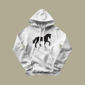 May include: A white hooded sweatshirt featuring a black silhouette of a horse in a trotting pose centered on the chest. The garment includes a front kangaroo pocket, long sleeves with ribbed cuffs, and matching white drawstrings at the neckline.