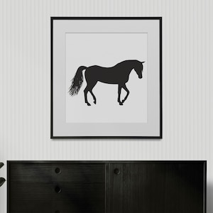 May include: A square framed wall art piece featuring a black silhouette of a horse standing in profile against a solid light gray background. The horse is depicted with its head slightly lowered and its tail flowing, enclosed in a thin black frame.