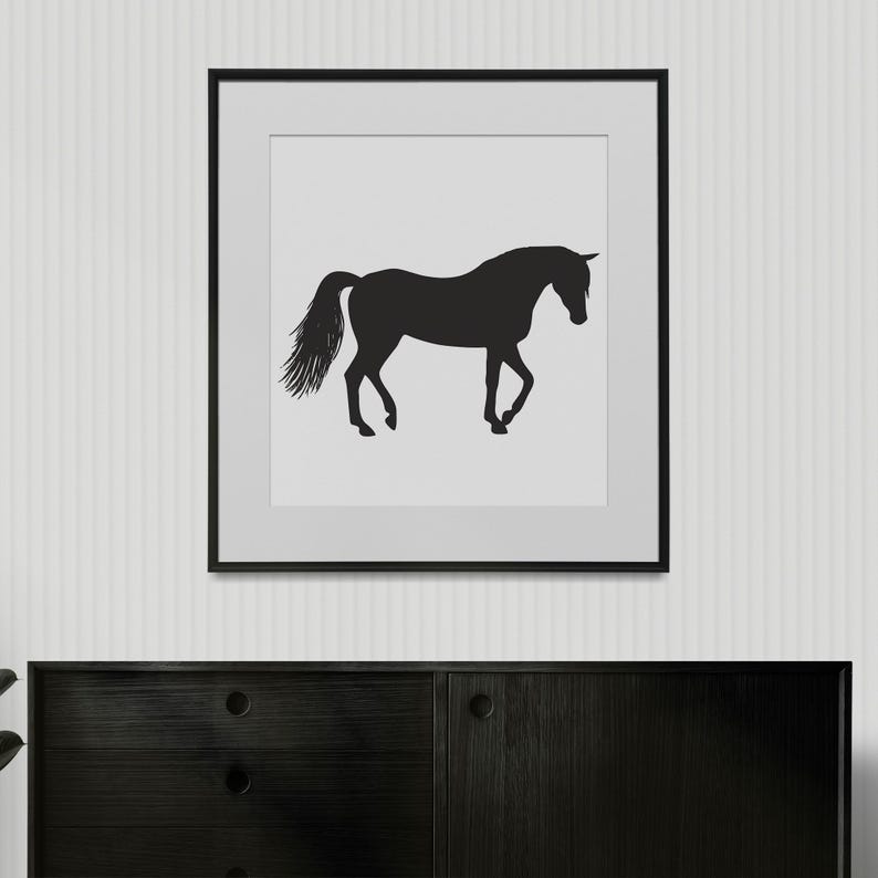 May include: A square framed wall art piece featuring a black silhouette of a horse standing in profile against a solid light gray background. The horse is depicted with its head slightly lowered and its tail flowing, enclosed in a thin black frame.