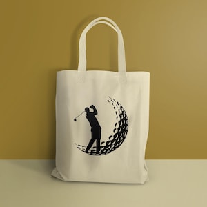 May include: A white canvas tote bag with a black silhouette of a golfer swinging a club, with a golf ball made of dimples behind him.