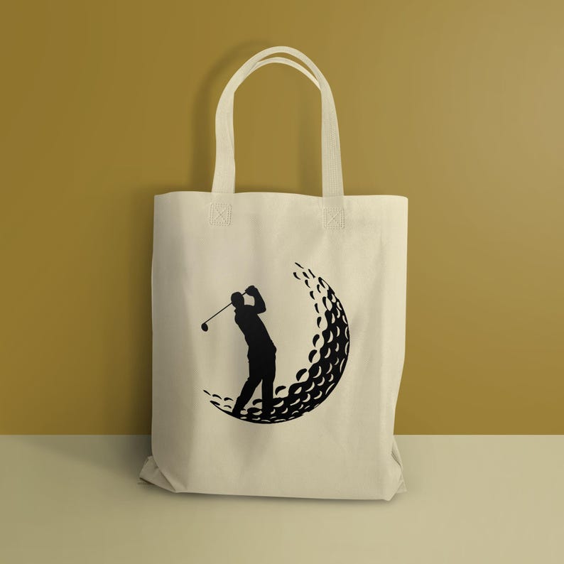 May include: A white canvas tote bag with a black silhouette of a golfer swinging a club, with a golf ball made of dimples behind him.