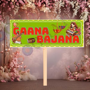 May include: A rectangular sign with the words "GAANA BAJANA" in red letters on a green background. The sign features illustrations of musical instruments and figures. The sign is held by a wooden stick, set against a floral backdrop.