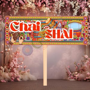 May include: A colorful sign with the words "Chai SHAI" in red, featuring intricate patterns and illustrations of drums and other cultural elements. The sign is held by a wooden stick, set against a backdrop of pink flowers.