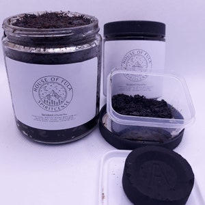 Può includere: Due barattoli di vetro con coperchi neri contenenti incenso marrone scuro. I barattoli hanno etichette bianche con il testo "House of Fula Spiritcense" e "Thourate (Choral Incense)". Un piccolo contenitore di plastica trasparente con un coperchio nero contiene una piccola quantità di incenso marrone scuro. Un piatto quadrato bianco contiene un disco di carbone nero.