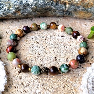 Peut inclure: Un bracelet en perles color&eacute;es avec un m&eacute;lange de pierres vertes, brunes, rouges et blanches. Le bracelet a des accents dor&eacute;s et un petit charme en m&eacute;tal.