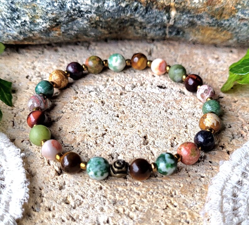 Peut inclure: Un bracelet en perles color&eacute;es avec un m&eacute;lange de pierres vertes, brunes, rouges et blanches. Le bracelet a des accents dor&eacute;s et un petit charme en m&eacute;tal.