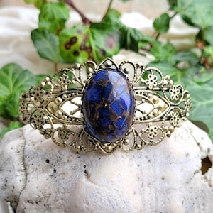 Op de afbeelding: Een gouden filigraan armband met een blauwe en bruine gemarmerde cabochon edelsteen.