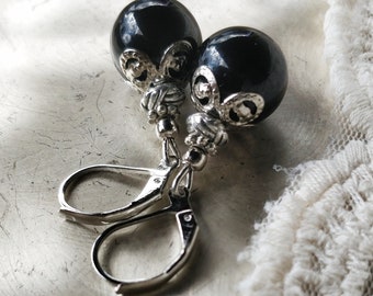 May include: A pair of silver earrings with black round beads and ornate silver accents. The earrings have a hook closure.