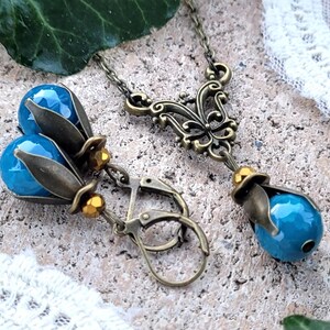 Pode incluir: Um colar com pingente de pedra turquesa e brincos combinando com um design de filigrana de bronze adornado. O colar apresenta uma corrente delicada e um pingente com um motivo de borboleta. Os brincos t&ecirc;m um design de gota com uma pedra turquesa e detalhes em bronze.