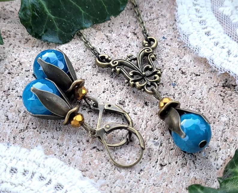Pode incluir: Um colar com pingente de pedra turquesa e brincos combinando com um design de filigrana de bronze adornado. O colar apresenta uma corrente delicada e um pingente com um motivo de borboleta. Os brincos t&ecirc;m um design de gota com uma pedra turquesa e detalhes em bronze.