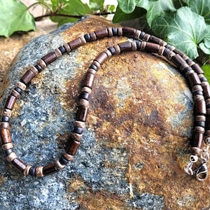 May include: A brown and black wooden beaded necklace with silver clasps. The necklace is made of natural wood and has a rustic look.