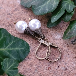 May include: A pair of white pearl earrings with antique gold-toned filigree accents and leverback closures.