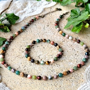 Peut inclure: Un ensemble de collier et de bracelet en pierres pr&eacute;cieuses multicolores. Le collier et le bracelet sont faits de diff&eacute;rentes pierres, notamment de l'&oelig;il de tigre, du jaspe et de l'agate. Les pierres sont enfil&eacute;es sur un cordon brun.