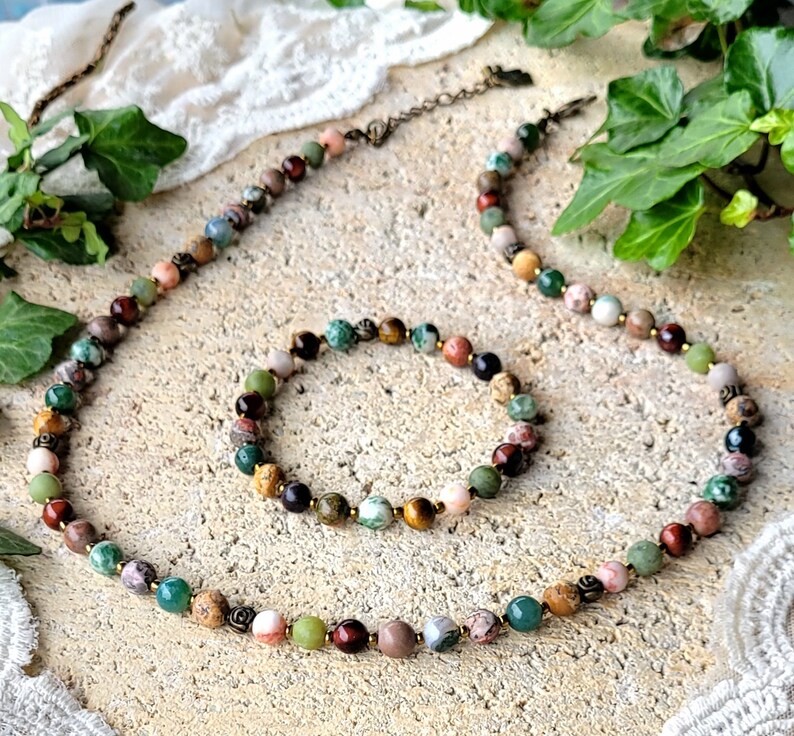 Peut inclure: Un ensemble de collier et de bracelet en pierres pr&eacute;cieuses multicolores. Le collier et le bracelet sont faits de diff&eacute;rentes pierres, notamment de l'&oelig;il de tigre, du jaspe et de l'agate. Les pierres sont enfil&eacute;es sur un cordon brun.