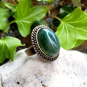 Op de afbeelding: Een ring met een groene agaat edelsteen en een bronzen zetting. De ring heeft een gedetailleerd, sierlijk ontwerp rond de steen.