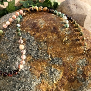 May include: A multi-colored gemstone necklace with a gold clasp. The necklace features a gradient of colors, starting with red, then orange, yellow, green, and finally blue. The necklace is made of round beads and is approximately 18 inches long.