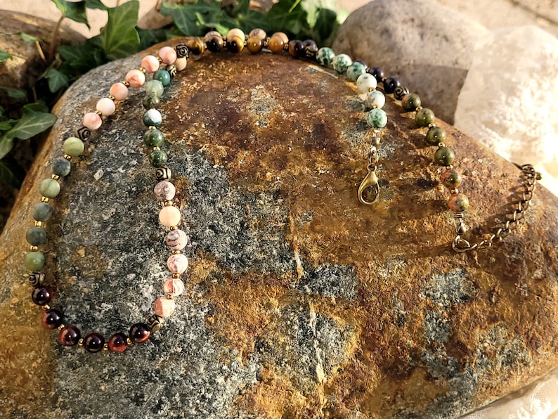 May include: A multi-colored gemstone necklace with a gold clasp. The necklace features a gradient of colors, starting with red, then orange, yellow, green, and finally blue. The necklace is made of round beads and is approximately 18 inches long.