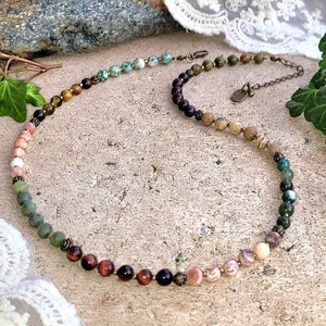 May include: A multi-colored gemstone necklace with a variety of stones including green, brown, and pink. The necklace is made with natural stones and has a simple design.