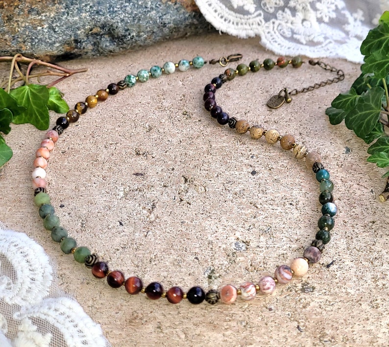 May include: A multi-colored gemstone necklace with a variety of stones including green, brown, and pink. The necklace is made with natural stones and has a simple design.