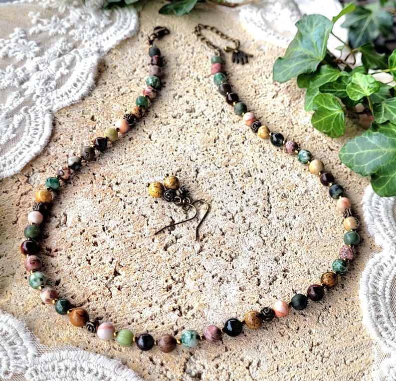 Peut inclure: Un collier de pierres multicolores avec une paire de boucles d'oreilles assorties. Le collier est compos&eacute; de pierres de diff&eacute;rentes nuances de brun, vert et rose. Les boucles d'oreilles sont faites des m&ecirc;mes pierres et ont un design simple.
