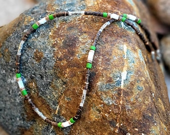 Può includere: Una collana di perline marroni, bianche e verdi con accenti argentati. La collana è realizzata con materiali naturali ed è un accessorio unico ed elegante.