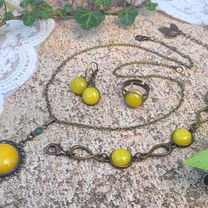 Könnte beinhalten: Ein Schmuckset mit Halskette, Ohrringen, Ring und Armband. Das Set hat eine Bronzefinish und gelbe Cabochon-Steine. Die Halskette hat einen großen Anhänger, und das Armband hat ein Unendlichkeitsdesign.