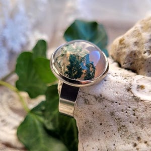 Könnte beinhalten: Ein silberner Ring mit einem runden, klaren Stein, der ein grünes und weißes Moosachat-Design zeigt.