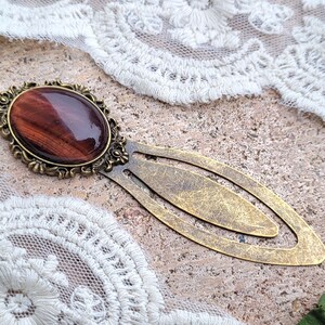 Op de afbeelding: Een gouden bladwijzer met een rode tijgeroog-steen in een decoratief frame. De bladwijzer heeft een ontwerp met dubbele lus.