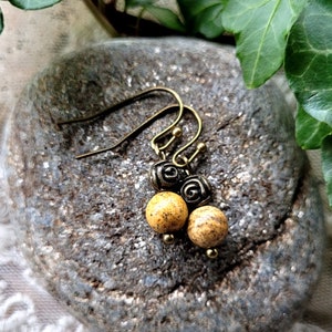 Peut inclure: Une paire de boucles d'oreilles en or avec des perles de pierre brunes et noires. Les boucles d'oreilles ont un design simple et sont parfaites pour tous les jours.