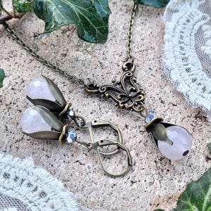 Pode incluir: Um conjunto delicado de colar e brincos de quartzo rosa com acabamento em bronze antigo. O colar apresenta um pingente floral com uma gota de quartzo rosa. Os brincos tamb&eacute;m s&atilde;o de forma floral com gotas de quartzo rosa.