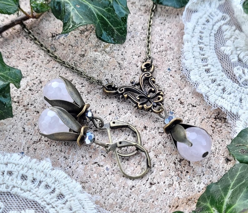 Pode incluir: Um conjunto delicado de colar e brincos de quartzo rosa com acabamento em bronze antigo. O colar apresenta um pingente floral com uma gota de quartzo rosa. Os brincos tamb&eacute;m s&atilde;o de forma floral com gotas de quartzo rosa.