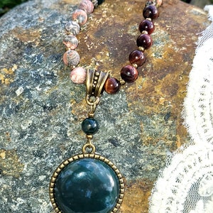 May include: A green agate gemstone pendant necklace with a brown and gold metal setting. The necklace is made with a variety of stones, including red tiger's eye, pink and green jasper, and green moss agate.