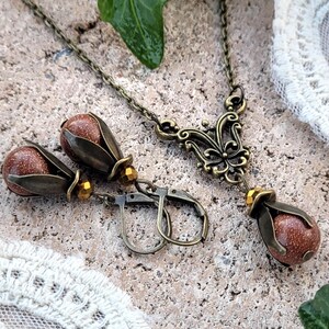 Pode incluir: Um conjunto de brincos e um colar com uma pedra marrom e detalhes dourados. Os brincos t&ecirc;m formato de l&aacute;grima e o colar tem um delicado pingente de borboleta.